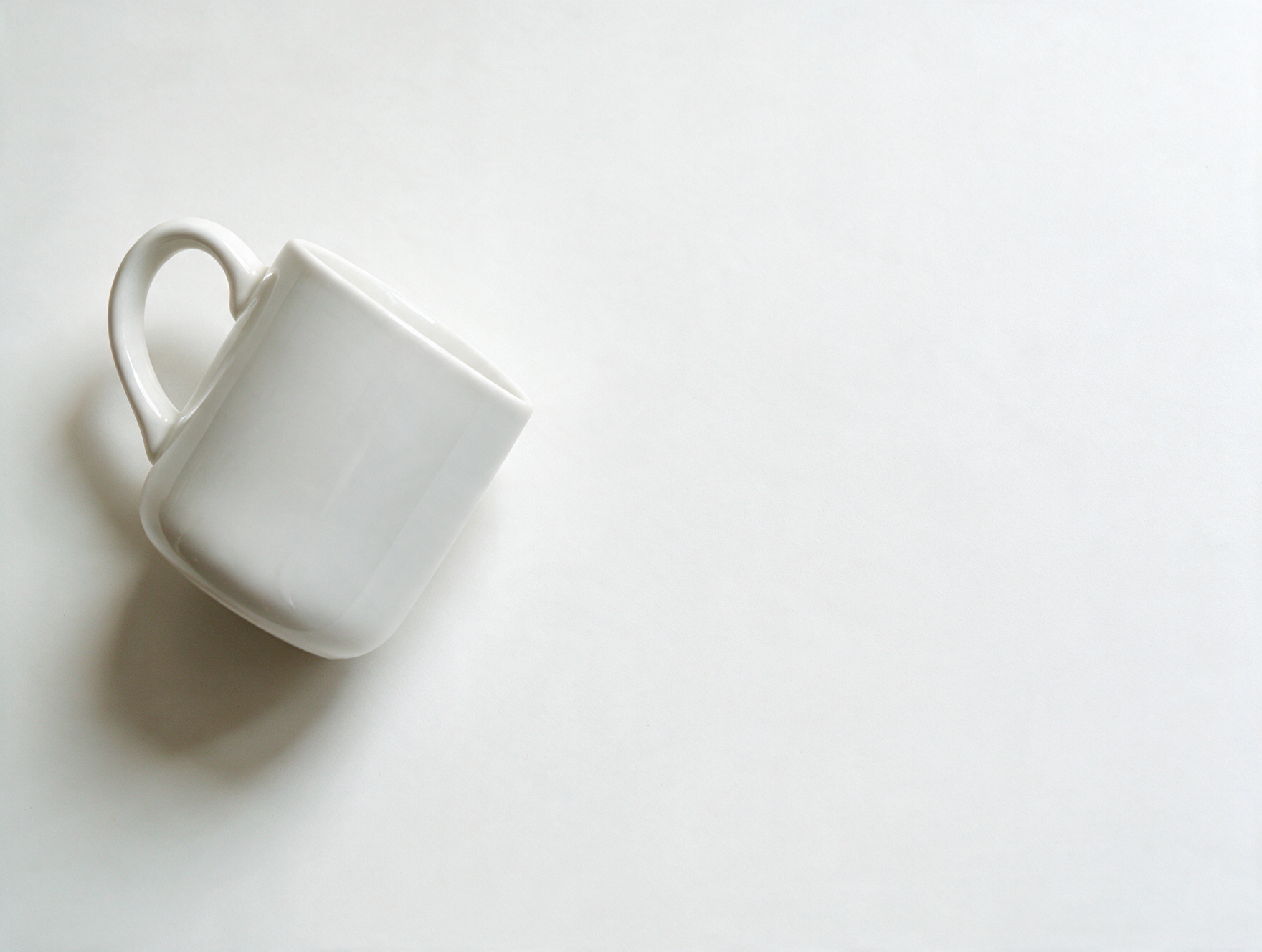 White ceramic mug on a clean white desk in soft natural light, product photography